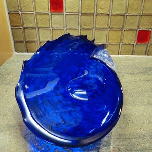 Könnte beinhalten: Eine kobaltblaue Glasschale mit einer wellenförmigen, organischen Form. Die Schale ist aus dickem Glas gefertigt und hat eine glatte, polierte Oberfläche.