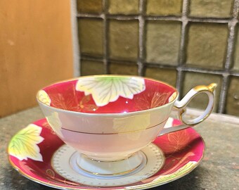 May include: A red and white teacup and saucer set with a gold trim and a floral design. The cup and saucer have a white interior and a gold rim.
