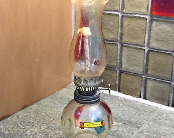May include: A vintage clear glass oil lamp with a rounded base and a flared top. The lamp has a metal collar and a wick inside. A sticker on the base reads "Dodge House Council Bluffs, Ia."