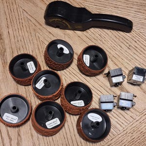 May include: A collection of rubber stamps and a black stamp handle on a wooden surface. The stamps are brown with black centers and white labels. The handle is black with the text "Stampin' Around".