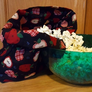 This popcorn bag made of apple theme fabric has just come out the microwave and popped kernels are pouring out of it into a green bowl. An example of what you can make with this sewing tutorial.