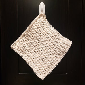 May include: A white crocheted dishcloth hanging on a white hook. The dishcloth is made with a simple stitch pattern.
