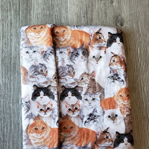 May include: A white fabric pouch with a repeating pattern of colorful cats. The cats are in various poses and have different fur colors and patterns.