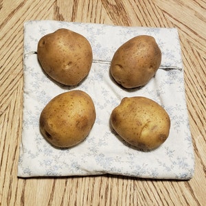 Four potatoes rest on a reusable microwave potato bag in the color of white with light blue floral design on the dining room table. This product is a sewing tutorial to make potato bags.