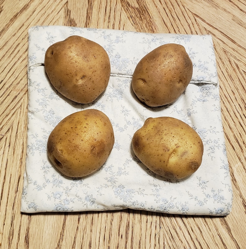 Four potatoes rest on a reusable microwave potato bag in the color of white with light blue floral design on the dining room table. This product is a sewing tutorial to make potato bags.