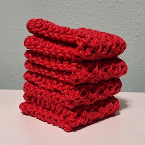 May include: A stack of five red crocheted dishcloths. The dishcloths are made with a simple stitch and are square in shape.