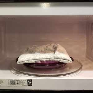 A filled reusable microwave potato bag on a microwavable plate inside a microwave oven in the color of white with light blue floral design. This product is a sewing tutorial to make potato bags.