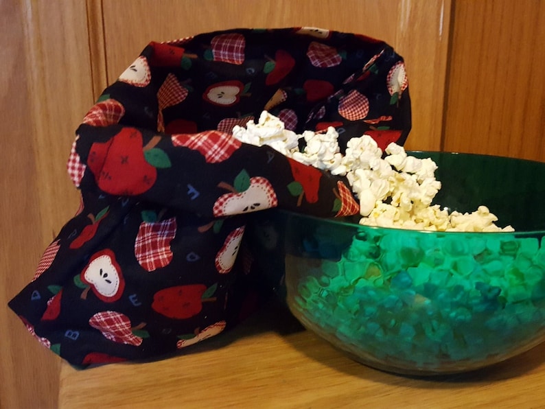 This popcorn bag made of apple theme fabric has just come out the microwave and popped kernels are pouring out of it into a green bowl. An example of what you can make with this sewing tutorial.