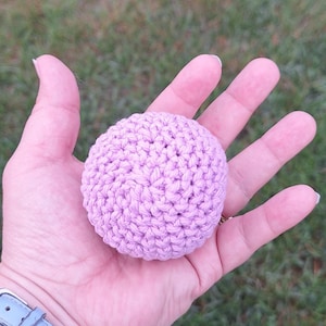 May include: A small, spherical object crafted from light purple yarn using a crochet technique. The item features a dense, textured stitch pattern that creates a uniform, rounded shape, showcasing the intricate loops of the fiber construction.