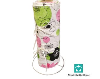 May include: A white fabric paper towel holder with a pink, green, and black floral pattern. The holder is made of fabric and has a metal ring at the top. The holder is on a white background.
