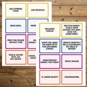 May include: Two sheets of paper with colorful rectangular boxes containing text. The text includes phrases like "Use Expiring Food," "Make Meal," "Organize Garage," and "Prep for Power Outage Task." The background is a wooden surface.