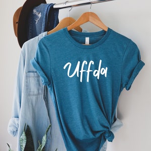 May include: A teal blue t-shirt with the word "Uffda" written in white on the front.