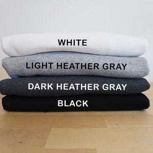 May include: A stack of four folded t-shirts in different colors: white, light heather gray, dark heather gray, and black.