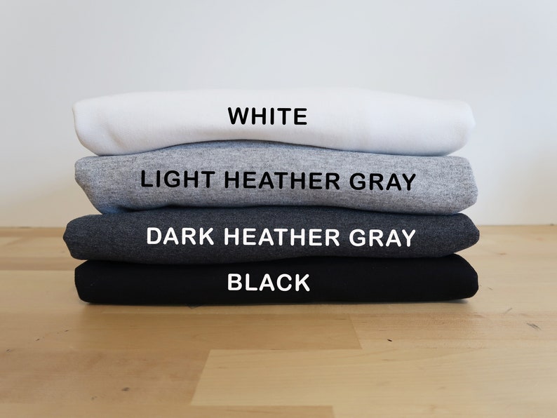 May include: A stack of four folded t-shirts in different colors: white, light heather gray, dark heather gray, and black.