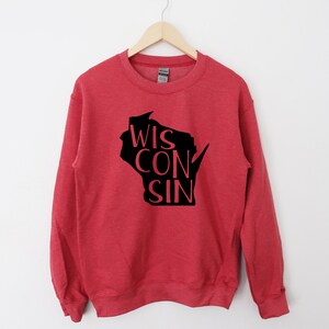 May include: Red sweatshirt with a black outline of the state of Wisconsin and the word "WISCONSIN" written inside the outline.