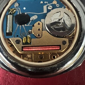 Puede incluir: Primer plano de la parte posterior de un reloj plateado con un mecanismo interno de color dorado. El reloj tiene un circuito impreso azul y una tapa de bater&iacute;a plateada con el texto "ROAMER" impreso en ella.