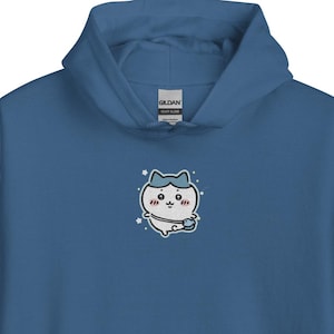 Puede incluir: Una sudadera con capucha azul con un bolsillo delantero y una capucha con cordón. La sudadera presenta un diseño de gato de dibujos animados bordado en el pecho. El gato es blanco con un sombrero azul y un lazo rosa.