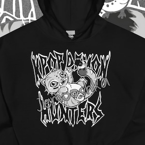 May include: Black hooded sweatshirt with a graphic design featuring a cartoon cat and the text "KPOP DEMON HUNTERS" in a stylized font. The website "Jemooshka.etsy.com" is printed at the bottom. The design is in black and white.