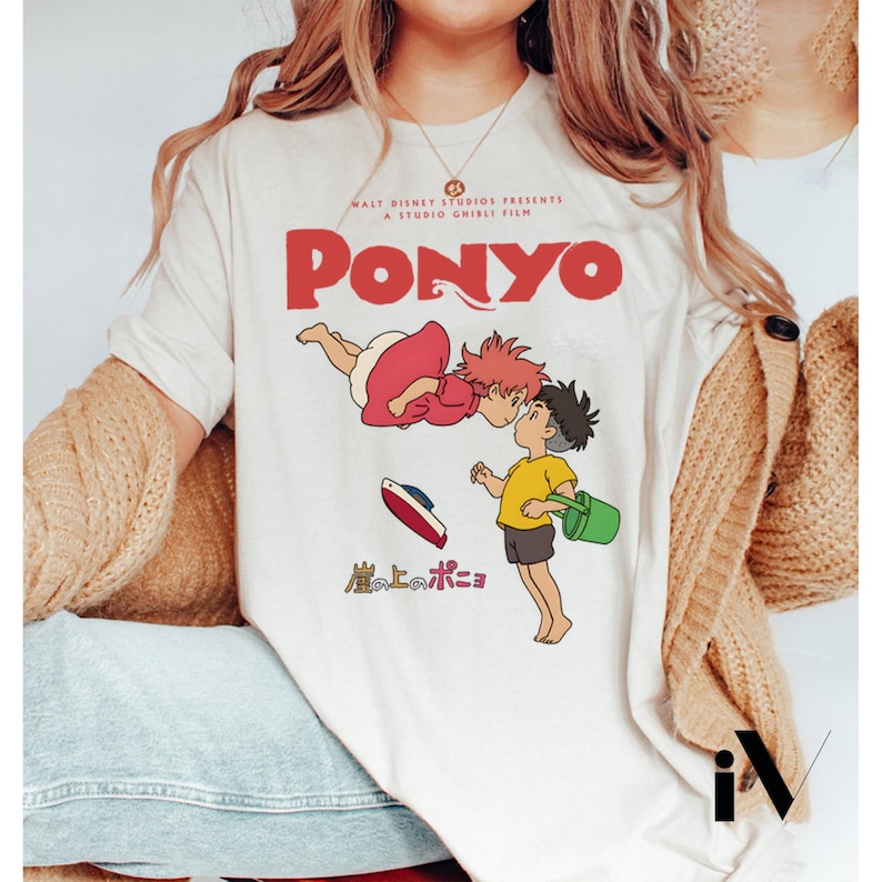 May include: Cream-colored t-shirt featuring a graphic from the animated film "Ponyo." The design includes the title "Ponyo" in red, along with illustrations of the characters. The shirt also displays the text "Walt Disney Studios Presents A Studio Ghibli Film."