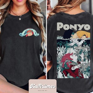 May include: Dark grey t-shirt with a small cartoon graphic on the front and a larger illustration on the back. The front graphic shows a character under a blue blanket. The back features the word "PONYO" and a colourful anime-style illustration.