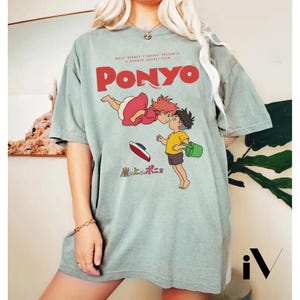 May include: A light green t-shirt featuring the animated film "Ponyo." The design includes the title in red, along with illustrations of the characters Ponyo and Sosuke. The shirt also has Japanese text and the Walt Disney Studios logo.