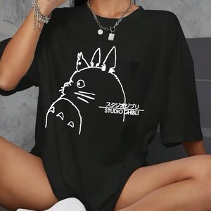 May include: Black t-shirt featuring a white outline of a cartoon character and the text "STUDIO GHIBLI" in English and Japanese. The shirt has short sleeves and a relaxed fit.