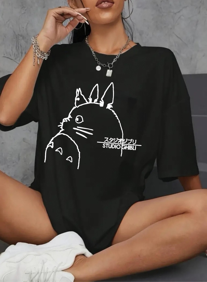 May include: Black t-shirt featuring a white outline of a cartoon character and the text "STUDIO GHIBLI" in English and Japanese. The shirt has short sleeves and a relaxed fit.
