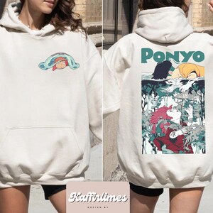 May include: Cream-coloured hoodie with a front pocket and hood. The front has a small cartoon graphic. The back of the hoodie features a larger graphic with the word "PONYO" and a detailed illustration of characters from the animated film.