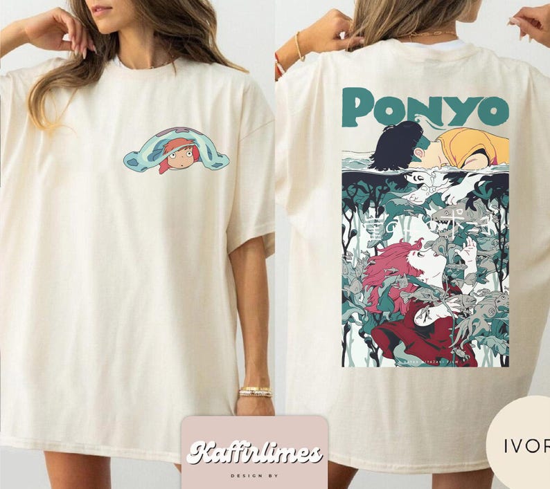 May include: Cream-coloured t-shirt with a front graphic of a cartoon character under a blue blanket. The back of the shirt features the word "Ponyo" in teal above a colourful anime-style illustration. The shirt has a relaxed, oversized fit.