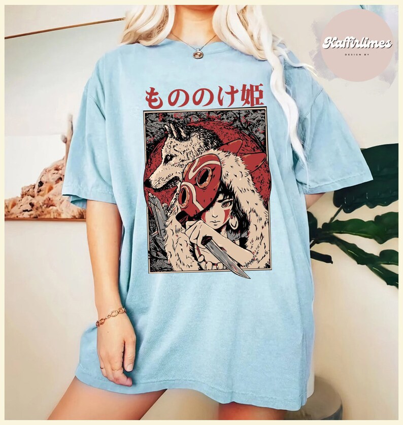 Op de afbeelding: Lichtblauw T-shirt met een afbeelding van een vrouw, een wolf en Japanse tekst. De afbeelding is rood, wit en zwart. Het shirt heeft een relaxte, oversized pasvorm.
