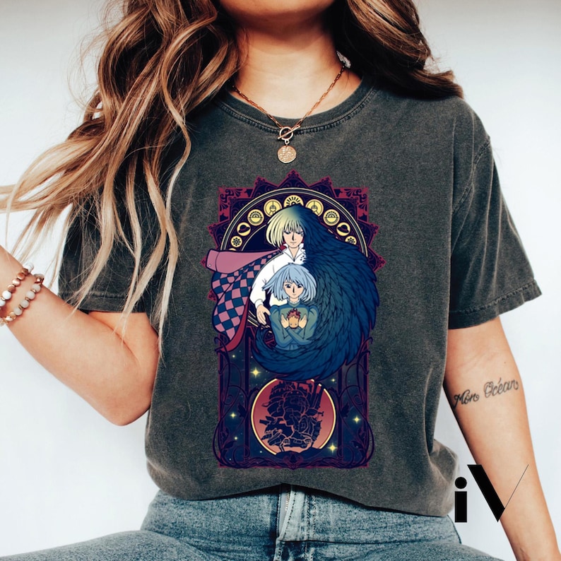 May include: Dark gray t-shirt featuring a colorful anime-style graphic. The graphic depicts two figures with long hair, one with blue hair and the other with blonde hair, within a decorative frame. The design includes purple, pink, and gold accents.