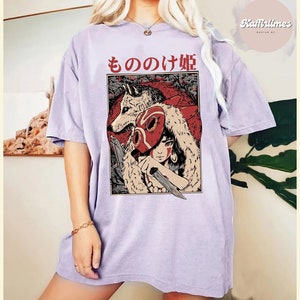 Op de afbeelding: Lichtpaars T-shirt met een afbeelding van een vrouw, een wolf en Japanse tekst. De afbeelding is rood, zwart en wit. Het shirt heeft korte mouwen en een losse pasvorm. De Japanse tekst luidt "もののけ姫".