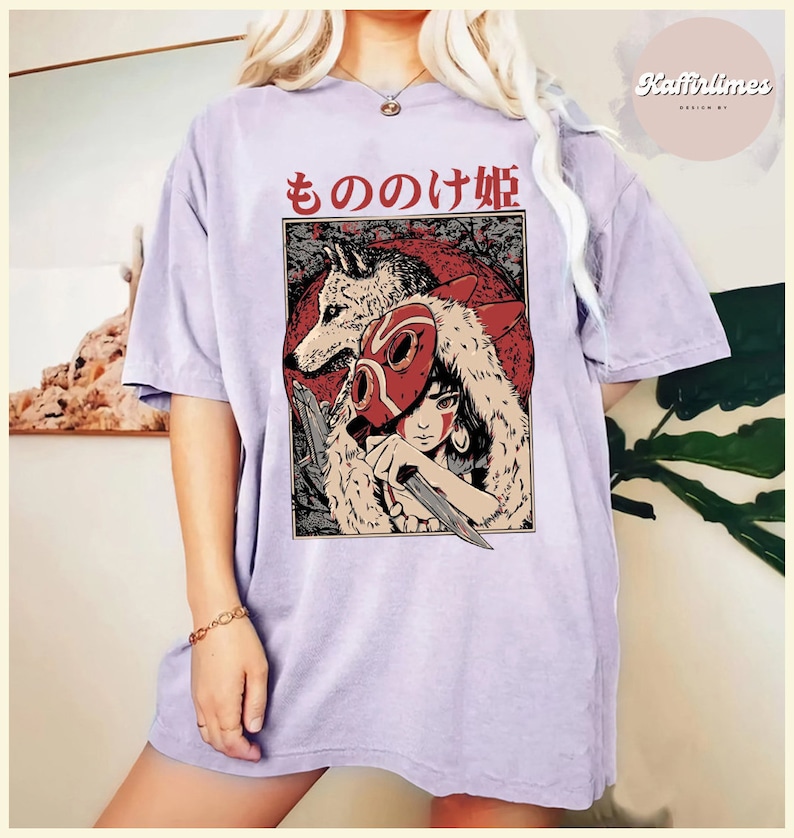 Op de afbeelding: Lichtpaars T-shirt met een afbeelding van een vrouw, een wolf en Japanse tekst. De afbeelding is rood, zwart en wit. Het shirt heeft korte mouwen en een losse pasvorm. De Japanse tekst luidt "もののけ姫".