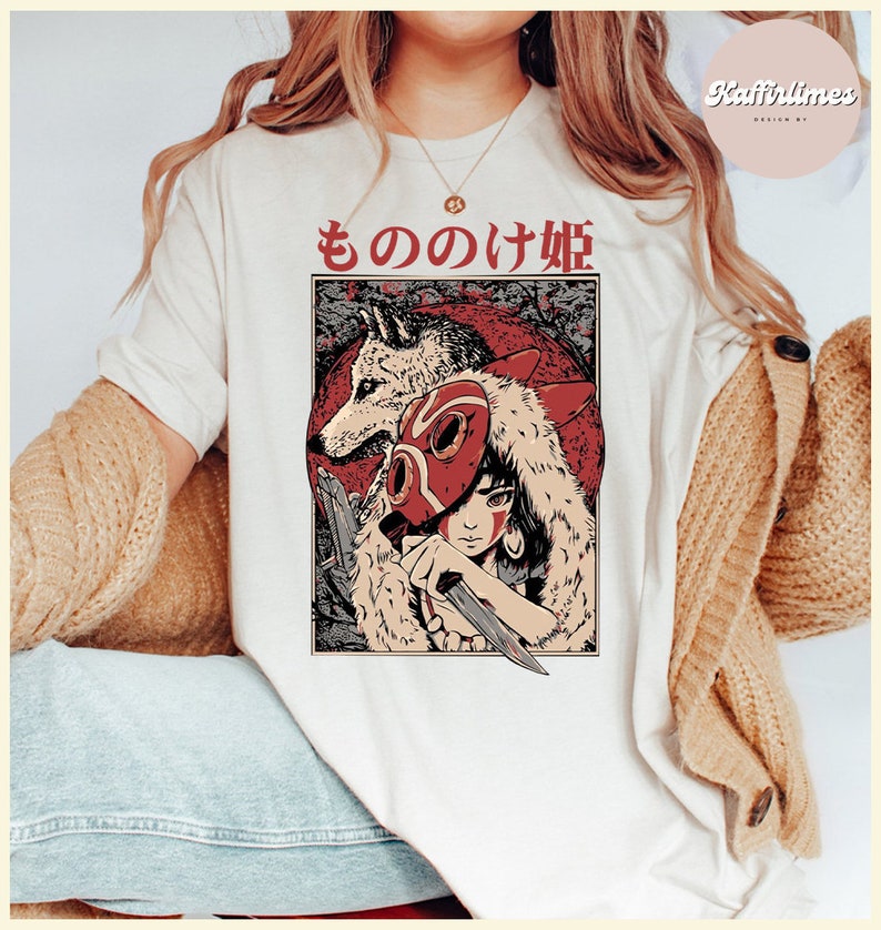 Op de afbeelding: Cr&egrave;mekleurig T-shirt met een Japanse illustratie in anime-stijl. De afbeelding bevat een wolf, een personage met een rood masker en Japanse tekst. Het ontwerp is geplaatst tegen een rode achtergrond met een bosachtig patroon.