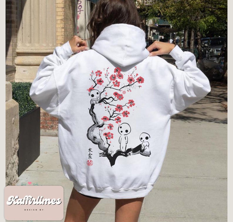 May include: White hoodie featuring a Japanese-inspired design. The back of the hoodie displays a black and white illustration of a tree with red blossoms and three small, white spirit figures. The hoodie has a drawstring hood and long sleeves.