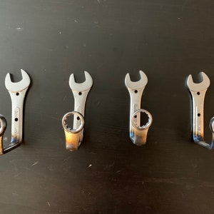 May include: Four silver wrench hooks mounted on a black surface. The wrenches are bent into a hook shape with the open end of the wrench facing up.