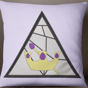 Op de afbeelding: Een paarse en gouden kroon met een scepter in een zwarte driehoek op een lavendelkleurig kussen.