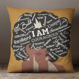 May include: A yellow throw pillow with a black and white illustration of a woman with an afro. The afro is filled with words describing positive attributes, including "strong", "resilient", "courageous", "unique", "sensational", and "hypnotic".