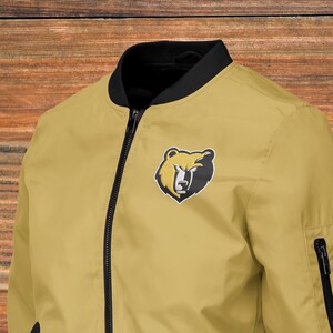 May include: A yellow bomber jacket with a black zipper and black trim. The jacket has a bear head logo on the left chest.