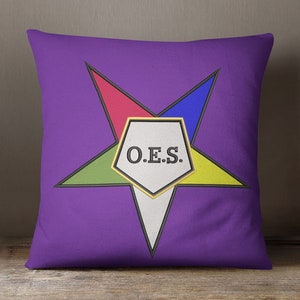 May include: Purple pillow with a five-pointed star in the center. The star is made up of four different colored triangles and a white pentagon in the center. The pentagon has the letters "O.E.S." in black.
