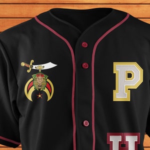 May include: Black baseball jersey with maroon piping and white lettering. The jersey has a gold and white emblem on the left chest with a sword and a crown. The letters "PHA" are on the right side of the jersey.