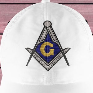 May include: White baseball cap featuring an embroidered emblem. The emblem includes a compass and square design with a gold "G" in the center, set against a blue background. The cap is made of a smooth fabric.
