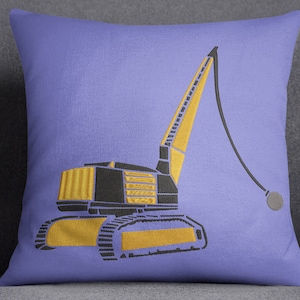 May include: A purple throw pillow with an embroidered design of a yellow and black construction crane with a black ball on the end of the arm.