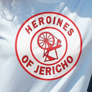 May include: White t-shirt with a red circle graphic that says "Heroines of Jericho" with a red spinning wheel inside the circle.