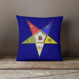 May include: A blue decorative pillow featuring a colorful star design with various symbols and a central emblem. The star is composed of red, green, yellow, blue, and white segments, each with a unique icon. The pillow is placed on a wooden surface.
