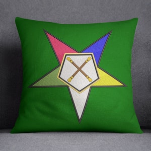 Puede incluir: Almohada verde con un diseño de estrella de cinco puntas en amarillo, rojo, azul y verde. La estrella tiene un centro blanco con dos bastones de madera cruzados.