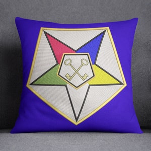 Puede incluir: Una almohada azul con una estrella de cinco puntas bordada en oro. La estrella está dividida en cuatro secciones, cada una de un color diferente: rojo, azul, verde y amarillo. En el centro de la estrella hay dos llaves doradas cruzadas.