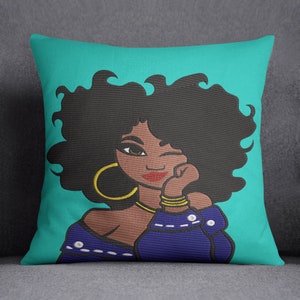 Puede incluir: Una almohada turquesa con una ilustración colorida de una mujer con cabello negro rizado, vistiendo una camisa azul y joyas de oro. Ella está guiñando un ojo y tiene su mano en su barbilla.