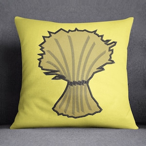 Puede incluir: Una almohada amarilla con un diseño bordado en negro de un manojo de trigo.