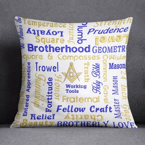 Può includere: Un cuscino bianco con un designo dorato e blu. Il design presenta una bussola e un quadrato, insieme a parole come "Fratellanza", "Temperanza", "Prudenza", "Fortezza", "Compagno d'arte" e "Amore fraterno".